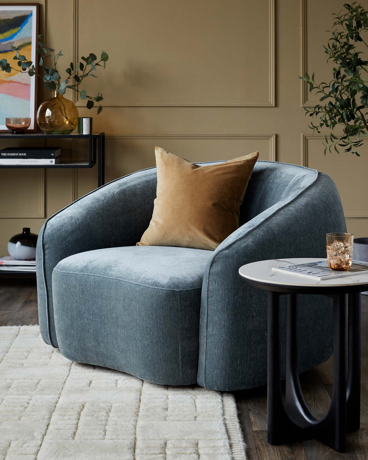 Stylish living room with a blue armchair, gold cushion and a round side table on a patterned rug.