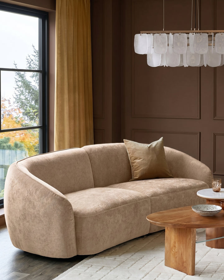 Zoey 3-seater sofa in champagne fabric with curved arms and rounded silhouette, displayed in a styled living room setting.