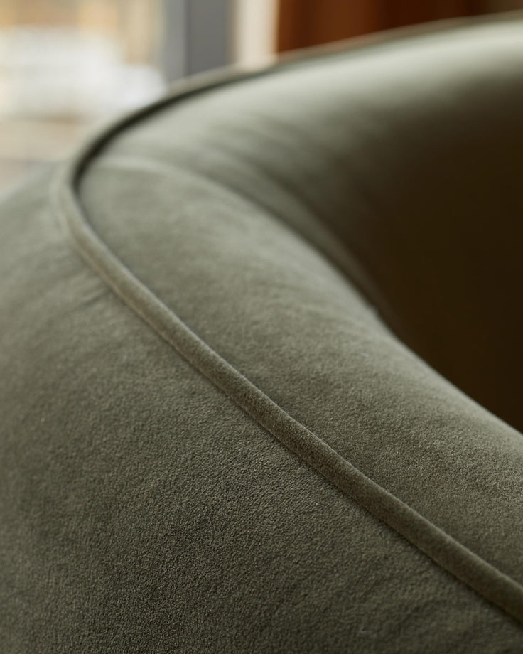 Close-up of a green velvet armchair, showcasing the plush fabric and curved design. Modern and stylish seating option.