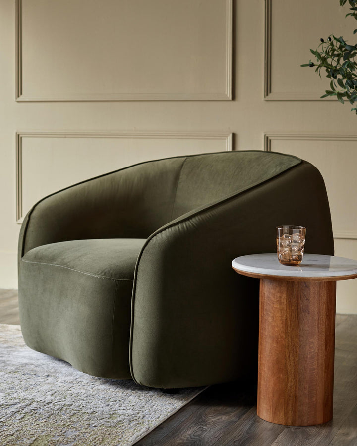 Green armchair beside round marble and wooden side table with a drink on top, in an elegant room.