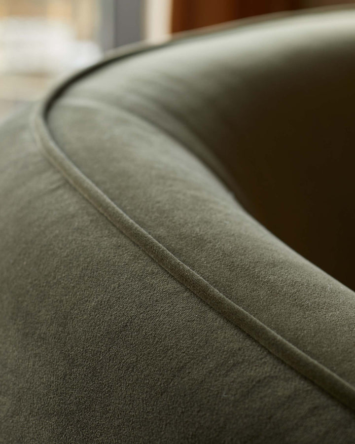 Close-up of an olive green, velvet-like armchair with a subtle piped seam, showcasing its texture and design.