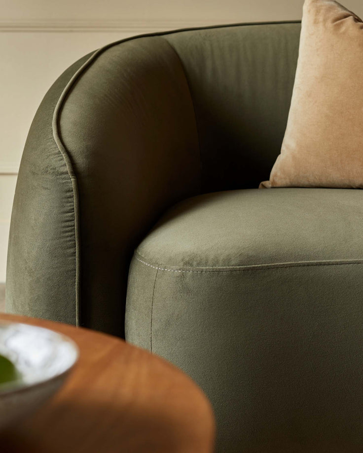 Close-up of a green velvet armchair with a neutral cushion, showcasing its luxurious texture and rounded design.