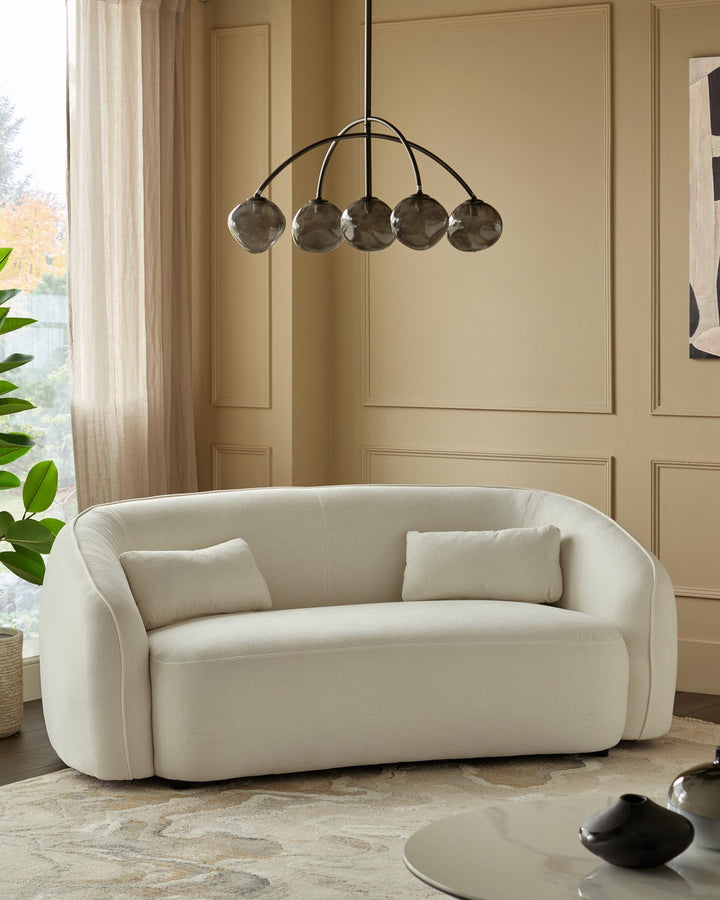 A stylish cream sofa with cushions, complemented by a unique light fixture, in a neutral-toned living space.