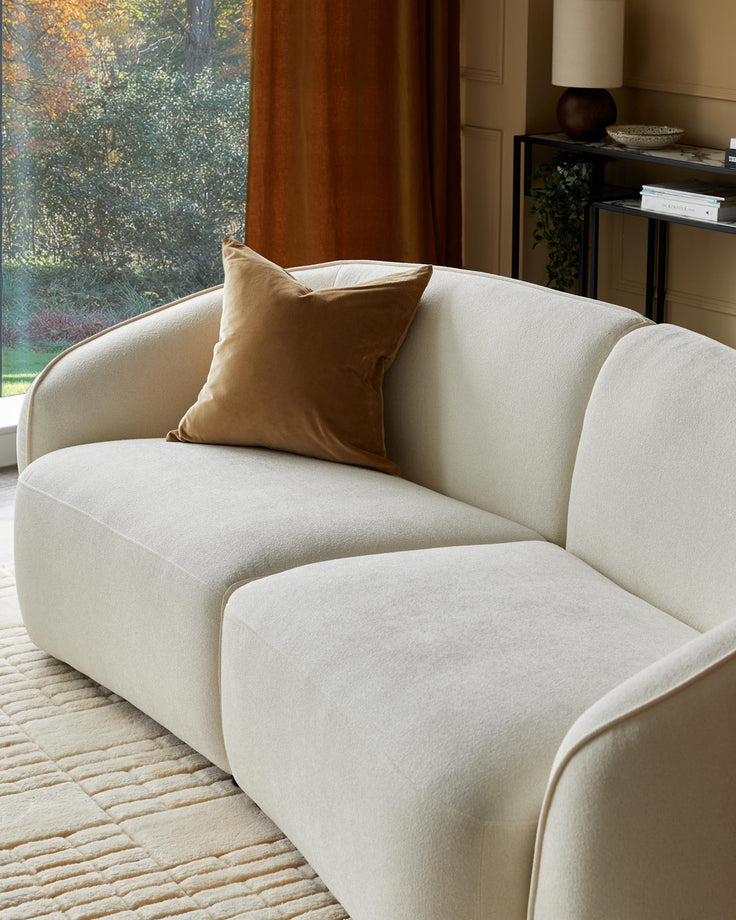 A modern, curved sofa with a brown velvet cushion, complemented by a stylish side table and lush outdoor view.