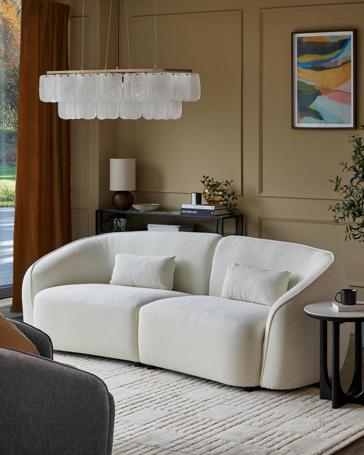 A modern living room with a curved sofa, marble side table, shelving unit and stylish light fitting.
