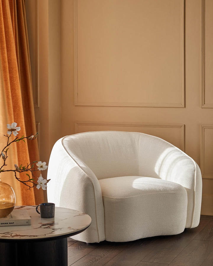 A cream boucle armchair sits beside a marble-topped coffee table, creating a cosy and inviting living space.