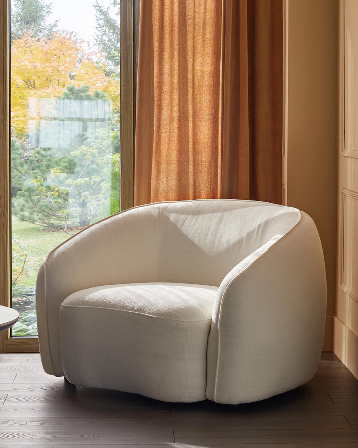 A stylish, cream-coloured armchair sits by a window, offering a cosy and inviting aesthetic to any living space.