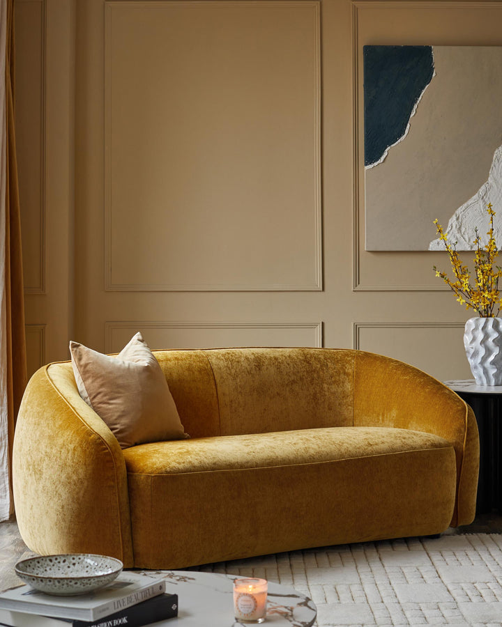 A stylish living room featuring a mustard velvet sofa, coffee table books, a rug and decorative art.