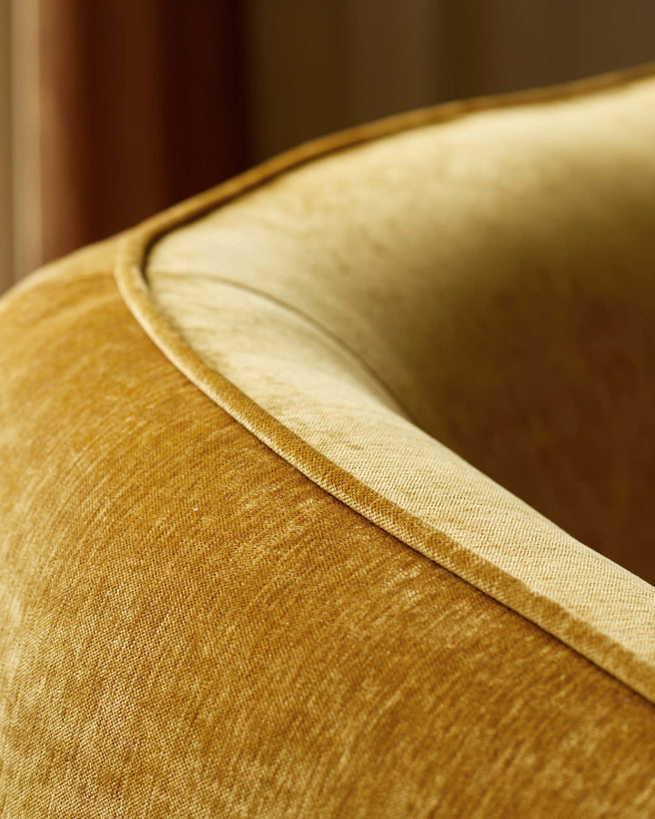 Close-up of a luxurious velvet armchair in a warm, golden hue, showcasing its plush texture and elegant design.
