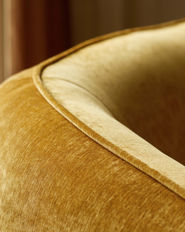 Close-up of a luxurious velvet armchair in a warm, golden hue, showcasing its plush texture and elegant design.