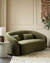 Stylish olive green curved sofa with cushions, side table with lamp, and framed abstract art in a modern living room setting.