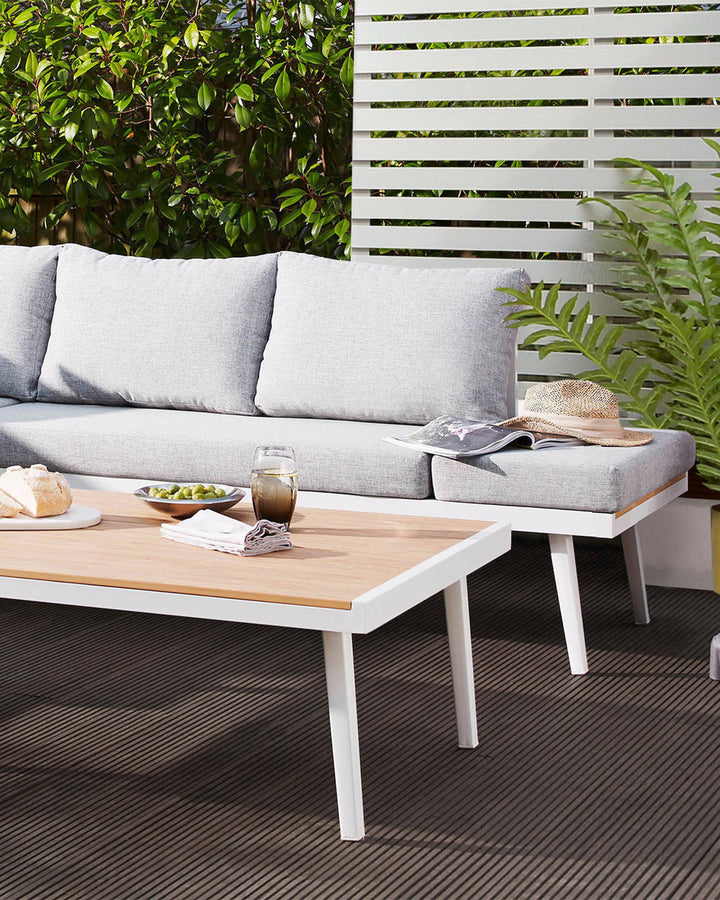Modern outdoor furniture set including a light grey upholstered sectional sofa with a chaise and a rectangular coffee table with a natural wood top and white legs.