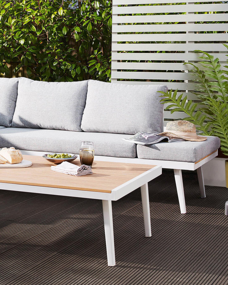 Modern outdoor furniture set including a light grey upholstered sectional sofa with a chaise and a rectangular coffee table with a natural wood top and white legs.