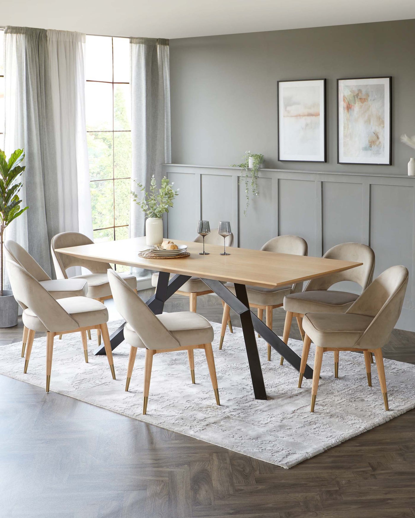 Elegant, modern dining room set featuring an oval wooden tabletop with striking black metal legs, surrounded by six plush, upholstered chairs in a cream fabric with light wood legs accented with gold tips. The set is presented on a textured white area rug.