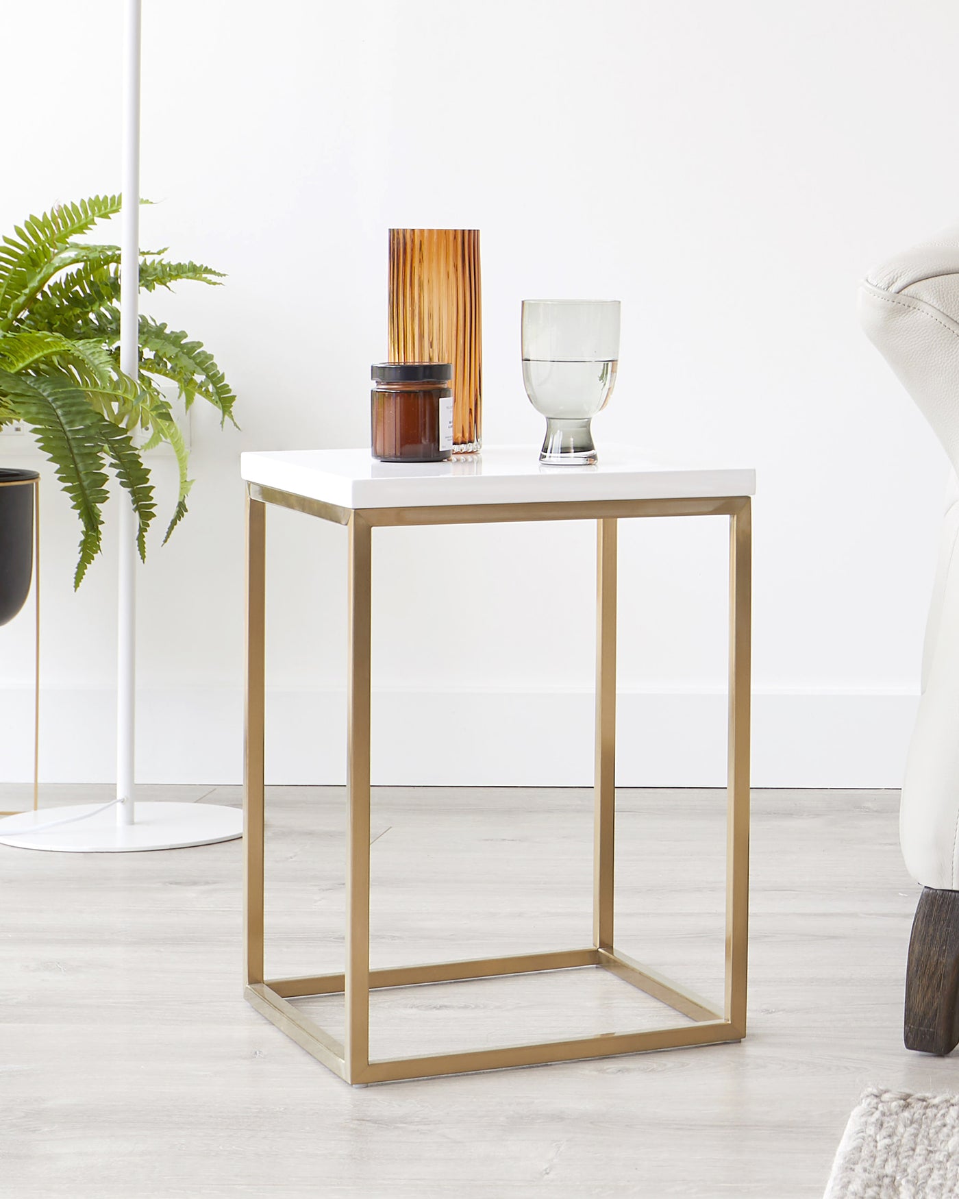 Modern minimalist side table with a white tabletop and a sleek gold metal frame, featuring decorative objects on top, set against a neutral interior backdrop.