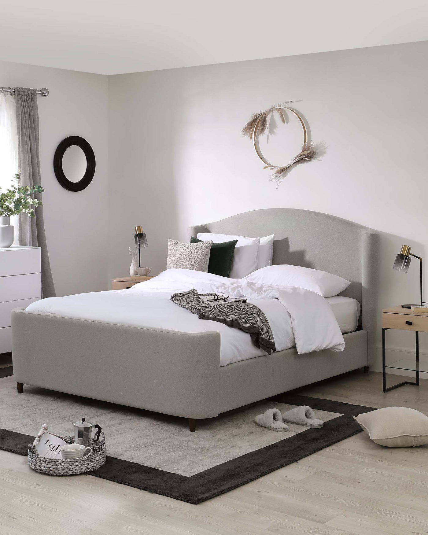 Modern bedroom furniture including a streamlined upholstered bed with a curved headboard in a light grey fabric, matching bedside tables with a simple, clean design, and a minimalist white dresser with sleek lines and white surface.