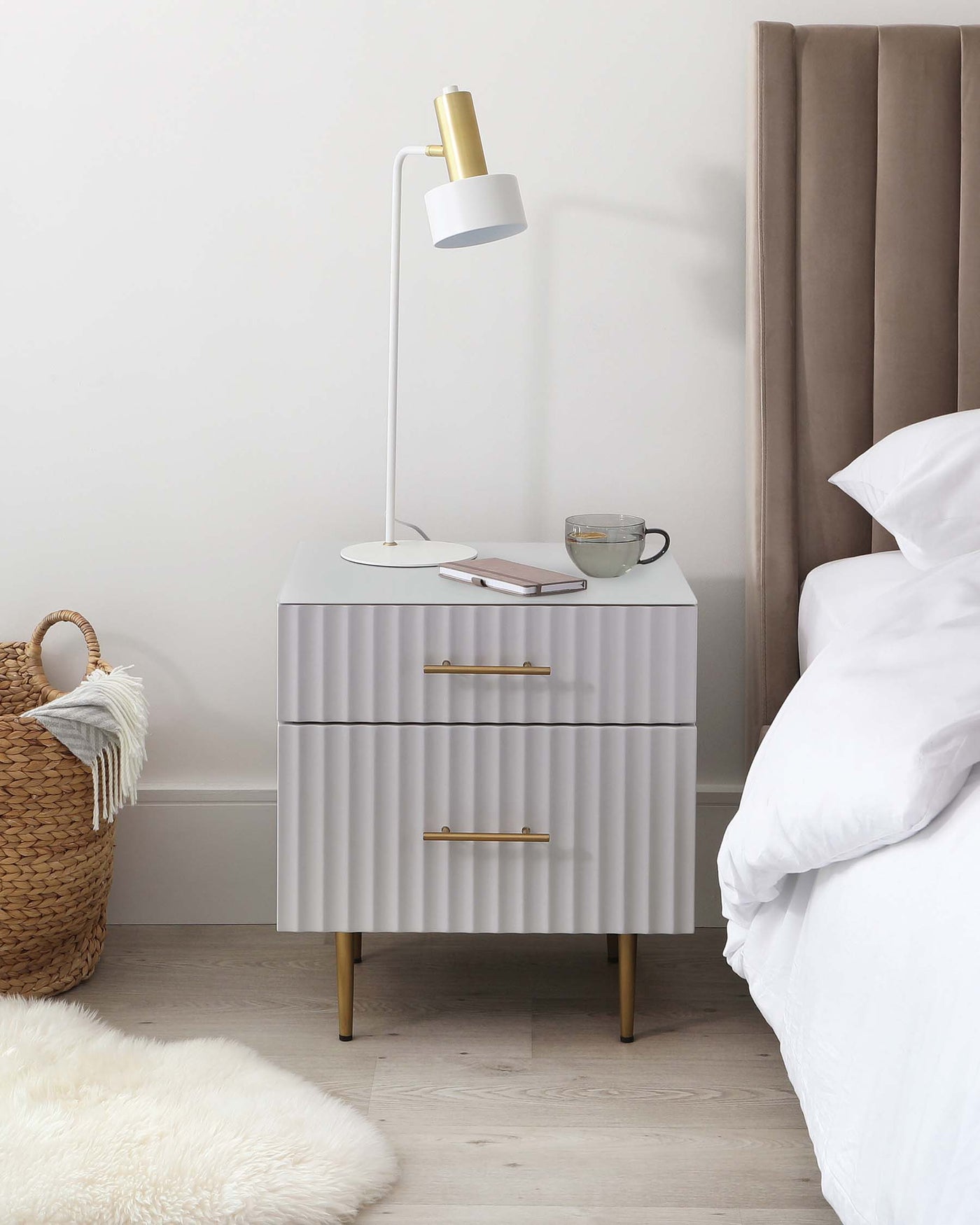 Elegant white ridged bedside table with brass accent handles and tapered legs, accompanied by a modern white and gold floor lamp.