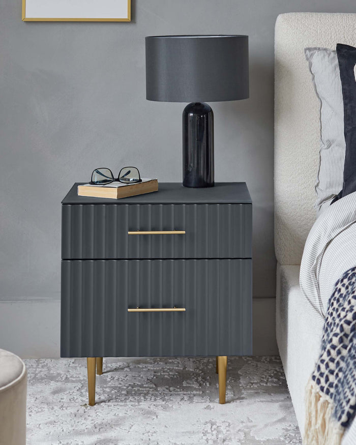Elegant charcoal-grey two-drawer nightstand with ribbed front detail and brass handles, supported by four tapered brass legs.