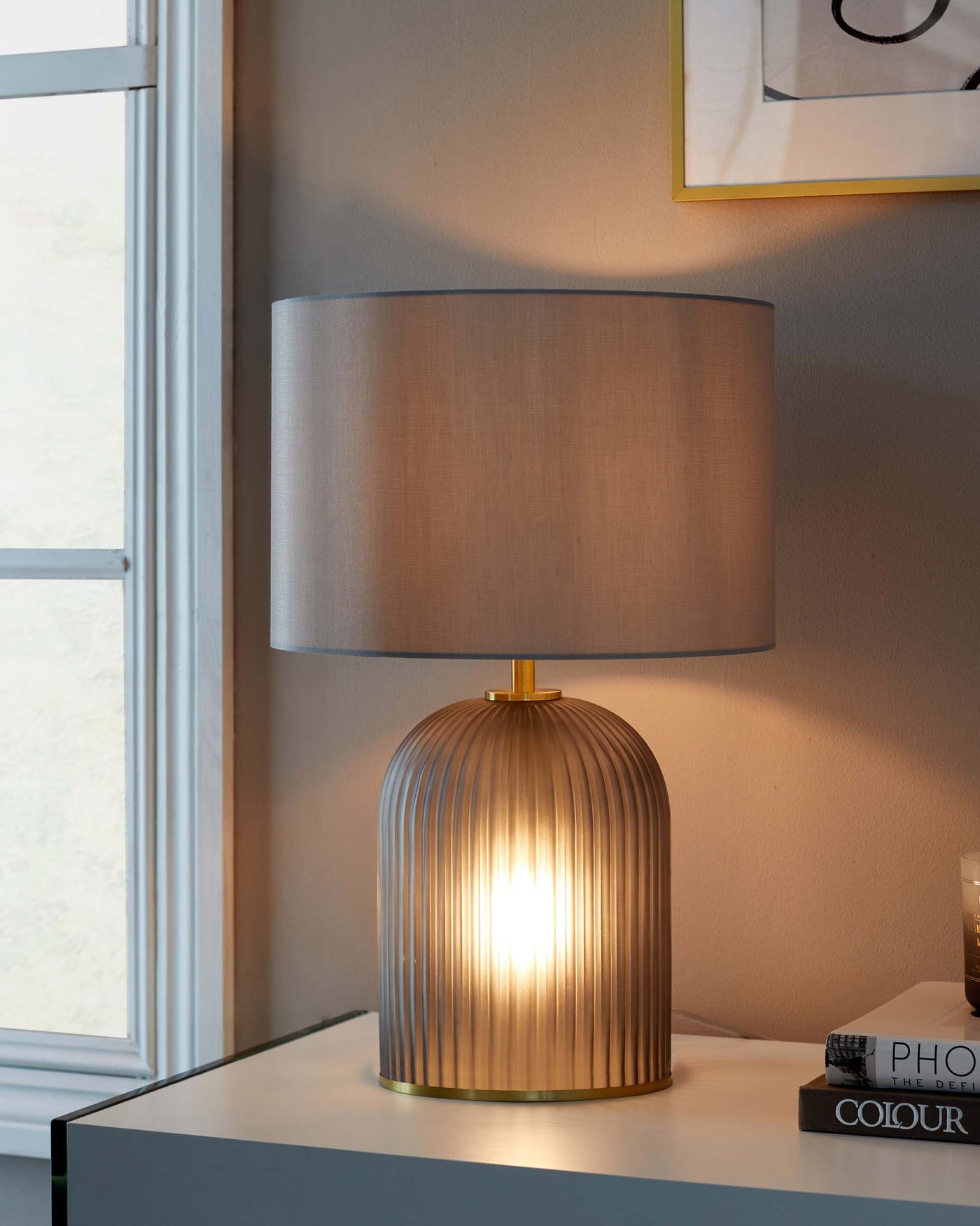 Table lamp with a cylindrical pleated metal base in a gold finish, topped with a broad cylindrical drum shade in a muted fabric.