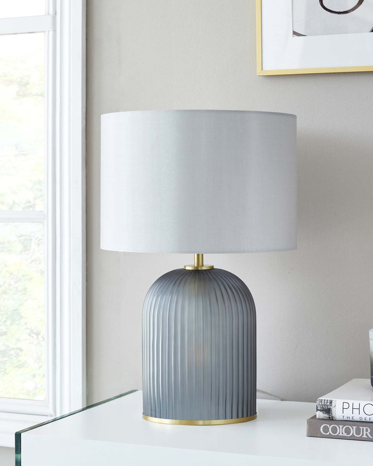 Elegant modern table lamp with a pleated grey ceramic base and a brass accent, topped with a grey fabric drum shade.
