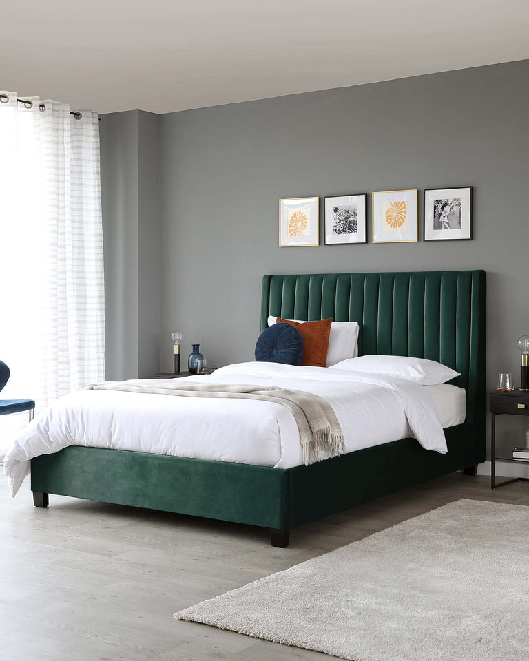 A contemporary bedroom featuring a luxurious emerald green velvet upholstered bed with a tall, channel-tufted headboard and low-profile frame. On each side of the bed, there are modern nightstands with reflective surfaces, each adorned with a table lamp and decorative items. The plush comfort of white bedding is complemented by a beige fringe throw and accent pillows in blue and orange. The bed is positioned on a soft grey rug, adding warmth to the sleek wooden flooring.