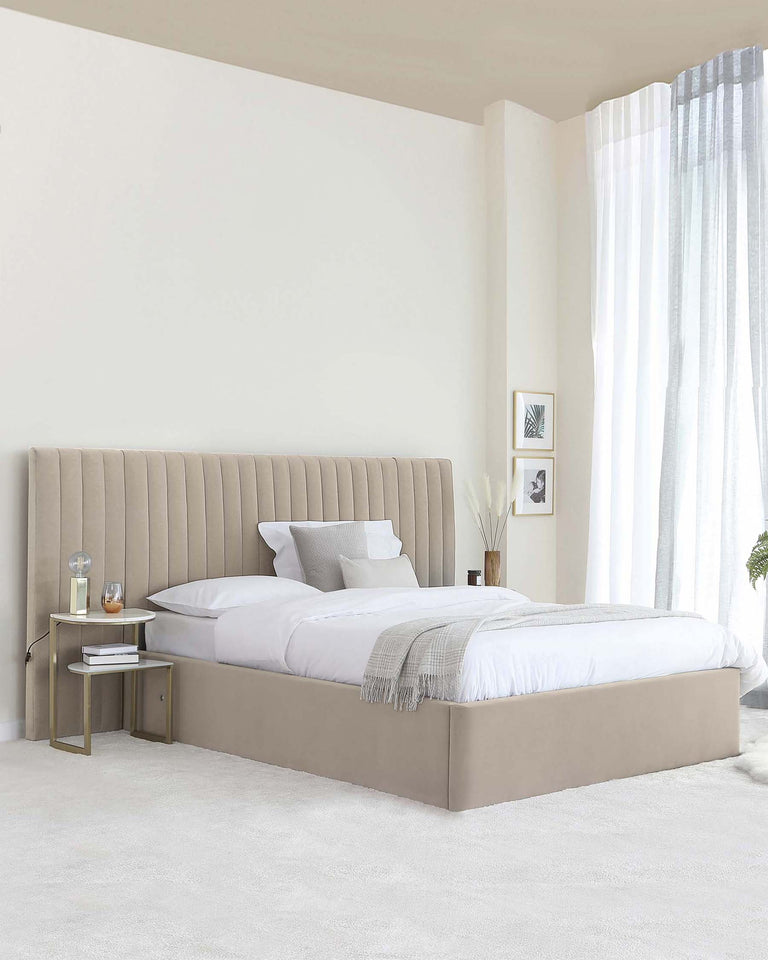 Elegant modern bedroom featuring a large upholstered platform bed with a tall, channel-tufted headboard in a soothing beige fabric. A minimalist side table with a gold frame and white shelves complements the bed on one side.
