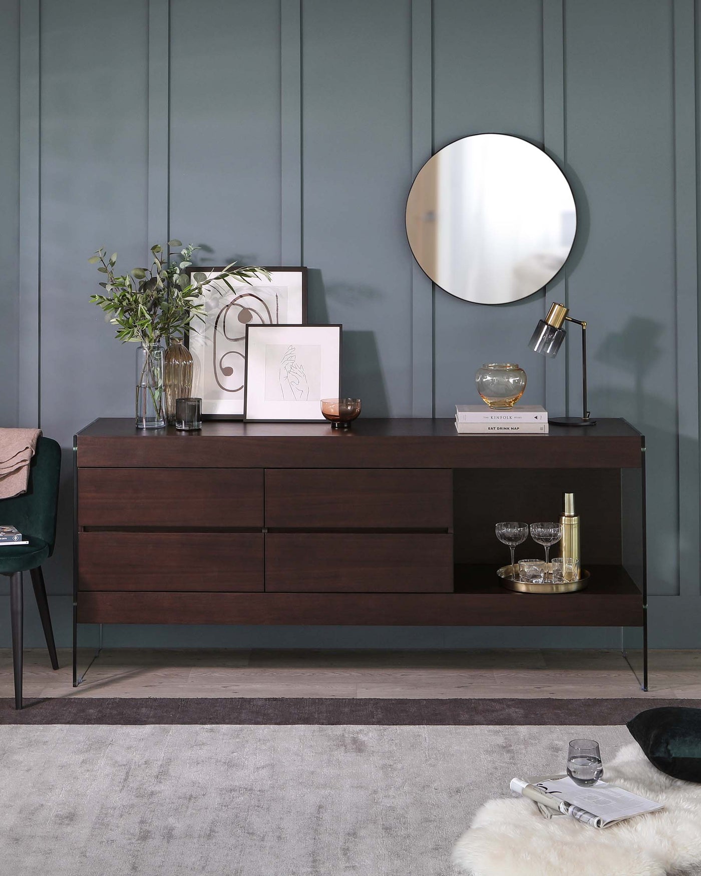 Contemporary dark wood sideboard with four drawers and open shelf, placed against a teal wall with decorative items and a round mirror above.
