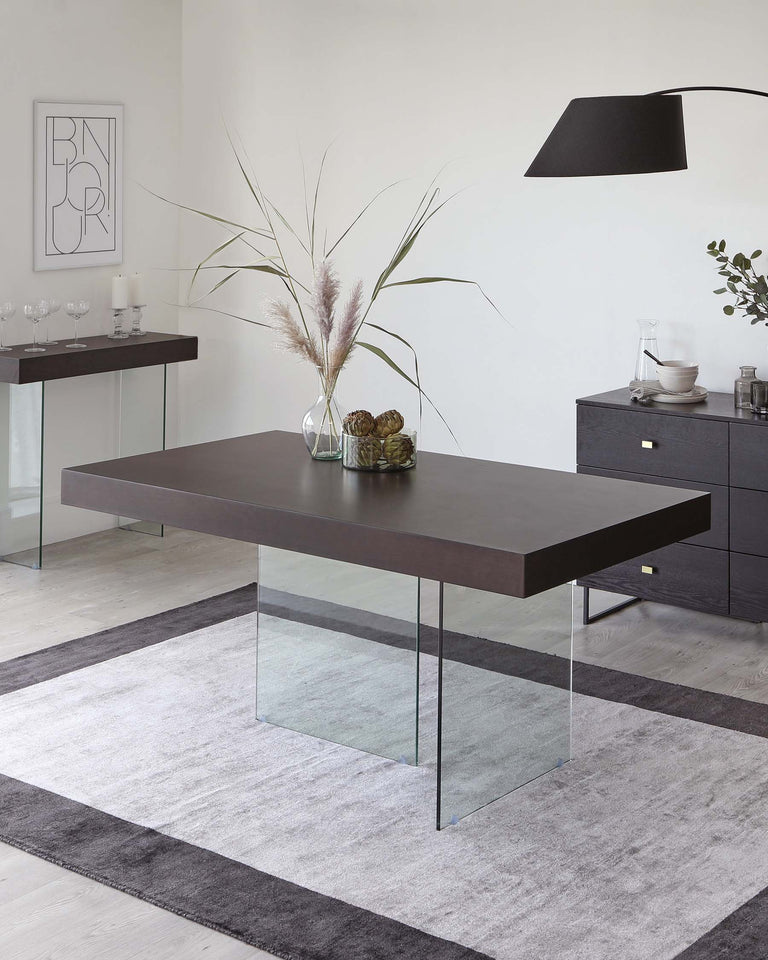 Modern minimalist furniture collection featuring a dark brown rectangular dining table with sleek glass legs, complemented by a matching sideboard with subtle handles, and a glass console table with a wooden top, all arranged on a gradient grey area rug.