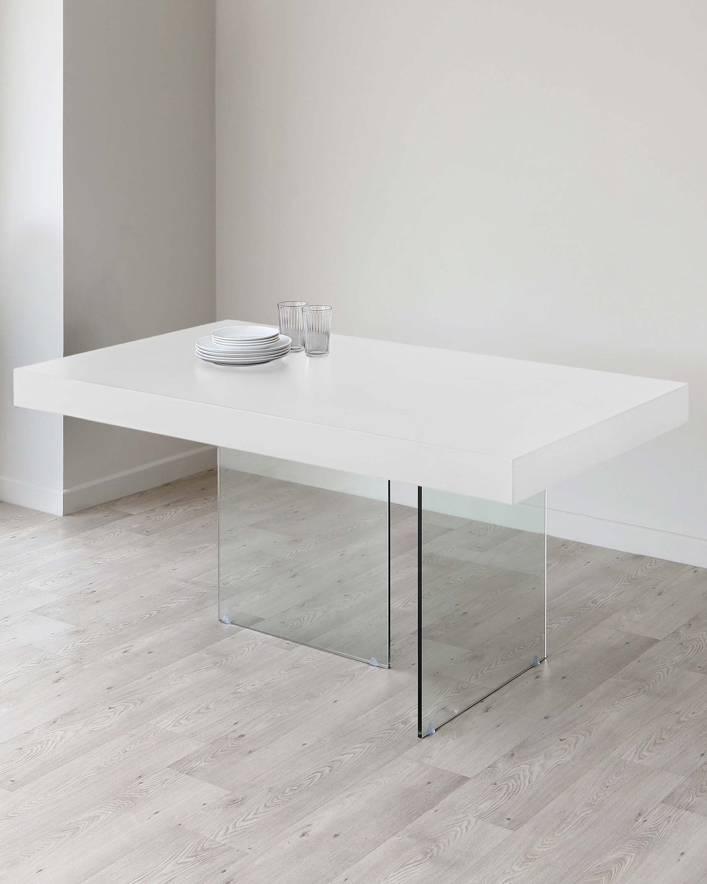 Modern minimalist white dining table with a sleek, rectangular top supported by a singular polished chrome pedestal on one end and a glass slab on the other, set against a clean, neutral background.