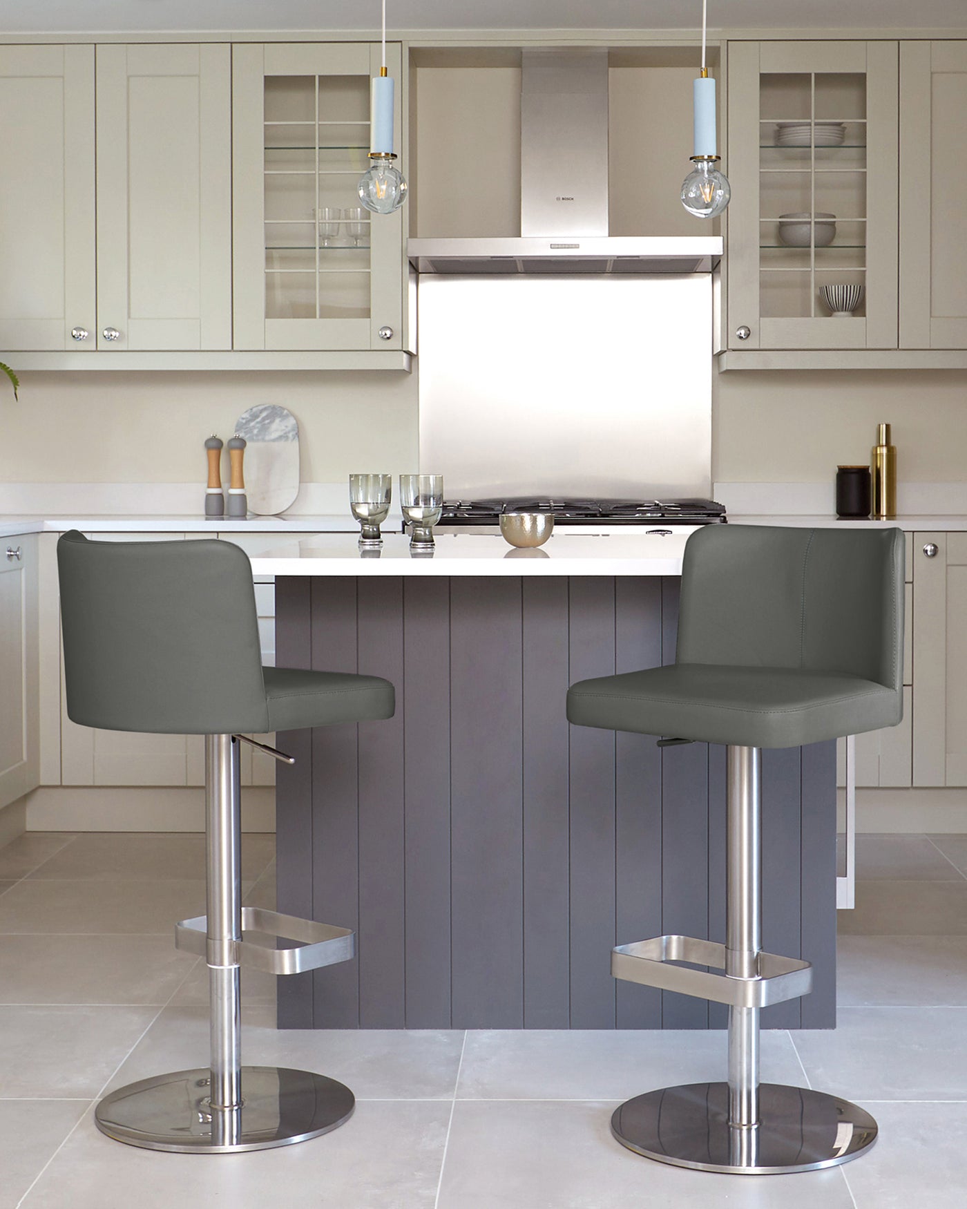 Two modern adjustable-height bar stools with dark grey upholstery and sleek chrome bases positioned at a kitchen island.