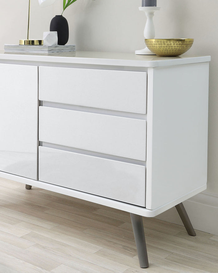 Modern minimalist white storage cabinet with four drawers featuring no-handle design and inclined metal legs.