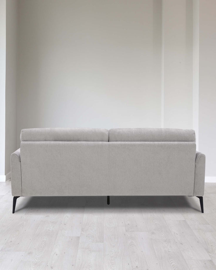 Modern light grey fabric three-seater sofa with clean lines, featuring black minimalist metal legs, positioned on a light wood floor against a soft white wall.