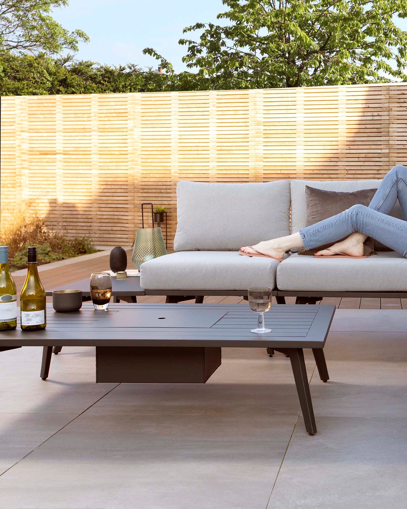 Modern outdoor furniture set featuring a charcoal grey, rectangular, low-profile coffee table and a matching corner sectional sofa with light grey cushions. The sofa's clean lines and minimalist design convey a contemporary aesthetic suitable for patios and outdoor lounging areas.