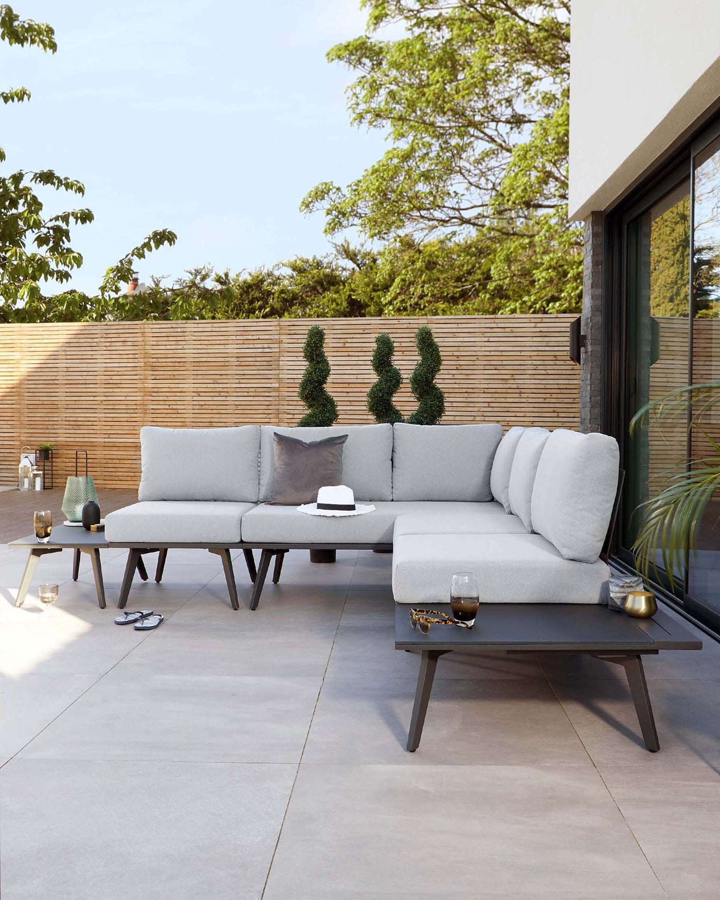 Modern outdoor sectional sofa in light grey with matching low-profile coffee table on a patio set against a natural backdrop.