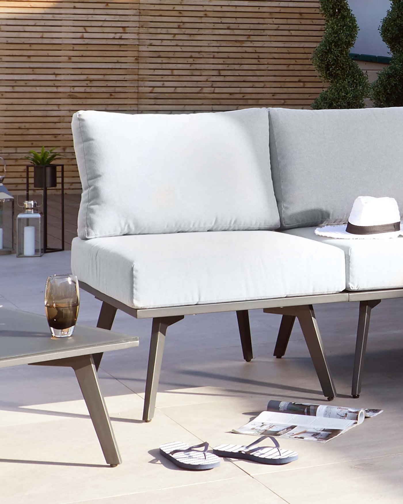 Modern outdoor two-seater sofa with light grey cushions and black angular metal frame, alongside a matching low-profile rectangular metal coffee table featuring a grey tabletop. The setting suggests a contemporary patio style.