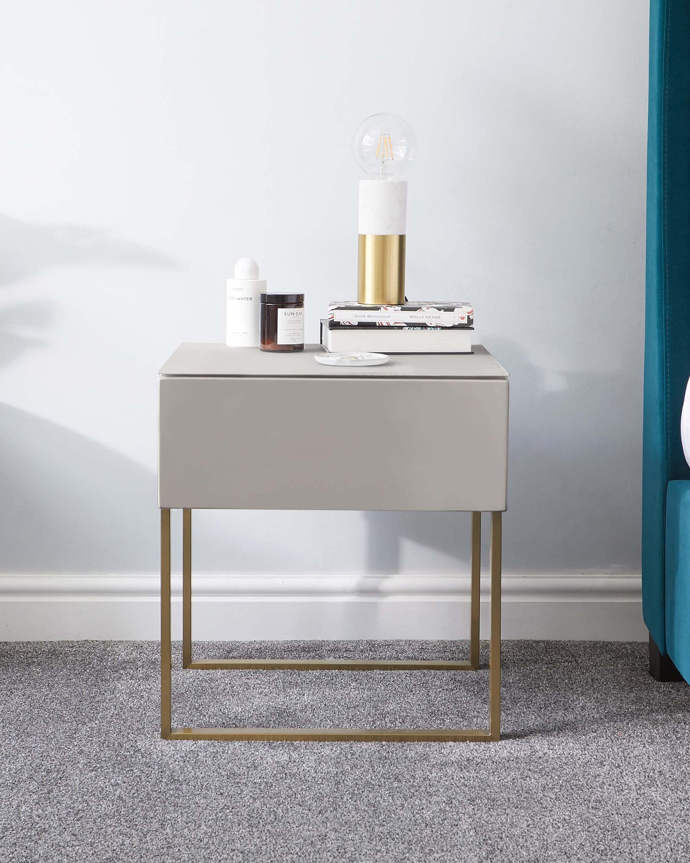 Modern minimalist nightstand with a smooth grey finish and sleek golden metal legs, styled with contemporary home accessories.