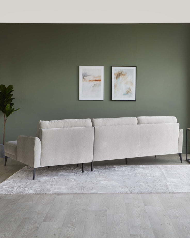 A modern, minimalist light beige three-seater sofa with clean lines and a sleek profile, set on slender black metal legs. The sofa is textured with a subtle woven fabric, presenting an understated and elegant look, perfect for a contemporary living space. It is positioned on a light grey and white patterned area rug over light hardwood flooring, enhancing the sofa's visual appeal.