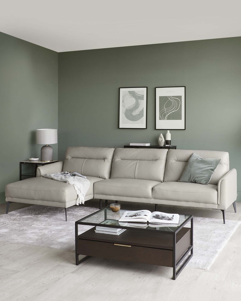 Modern living room featuring a light grey, contemporary L-shaped sectional sofa with metal legs, a dark brown rectangular coffee table with glass top and a lower shelf, and a black side table with a matching dark brown tabletop. The furniture is complemented by a minimalist white floor lamp and elegant decor items.
