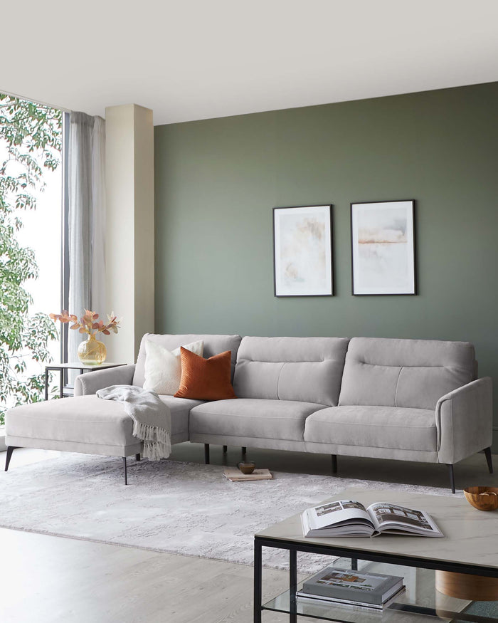 Stylish gray sectional sofa with orange accent pillow, glass coffee table, and decorative accessories in a modern living space.