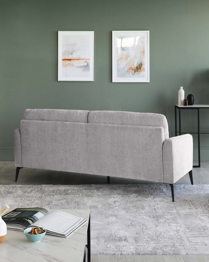 Modern light grey fabric sofa with clean lines and black tapered legs, positioned in a minimalist setting with a dark round side table featuring a matte finish and slender legs. A textured off-white area rug underlines the composition, enhancing the contemporary aesthetic of the space.
