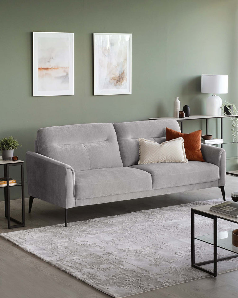 Modern furniture set including a grey three-seater fabric sofa with clean lines and tapered legs, accompanied by a minimalist black metal end table with a square top and lower shelf. A sleek black console table with a slim profile and several decorative items rests against the wall. A neutral-toned patterned area rug anchors the space.