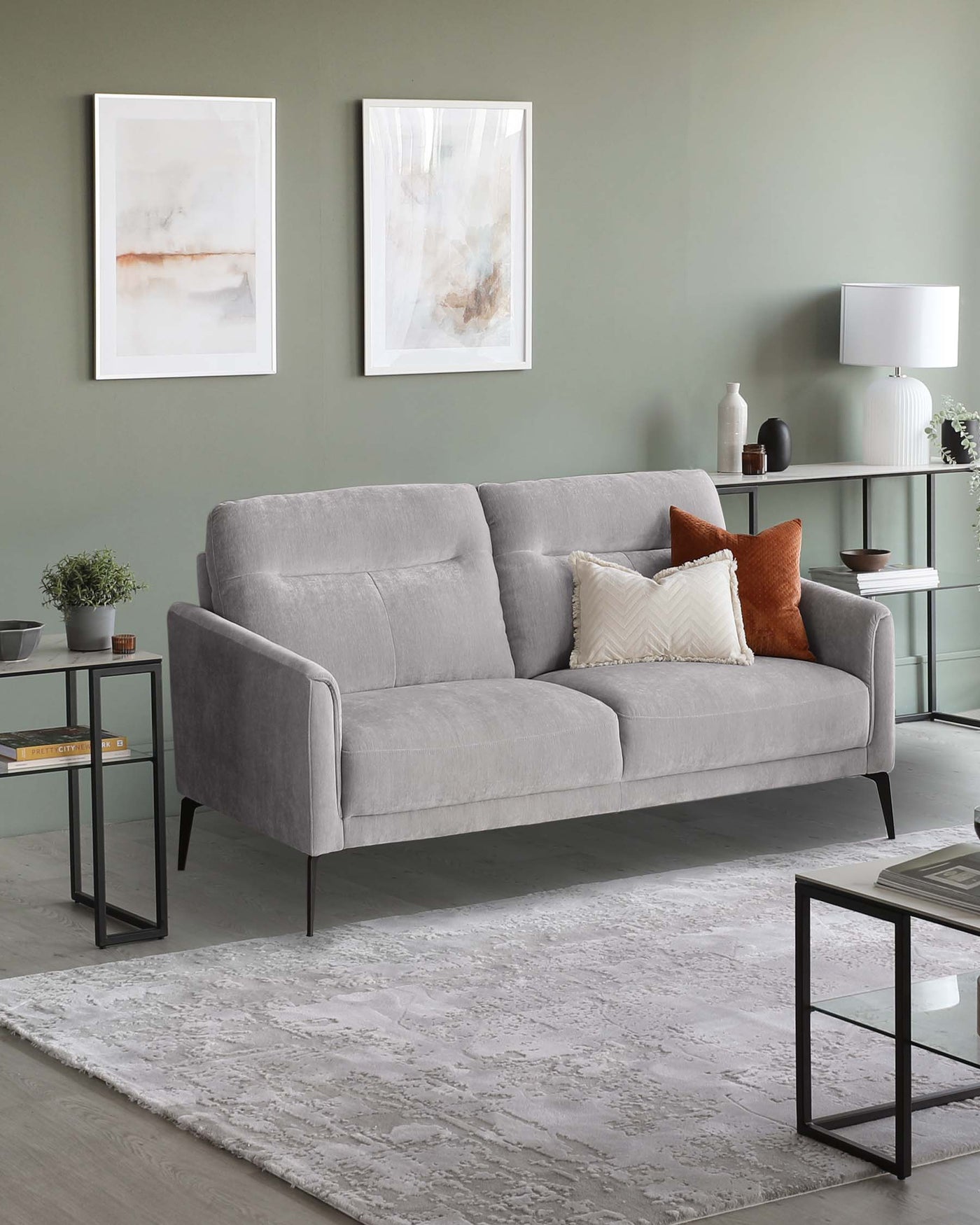Contemporary three-seater sofa in light grey fabric with sleek armrests and dark angled legs, flanked by two modern side tables with black metal frames and dark wood tops, set on a textured grey area rug over light hardwood flooring.