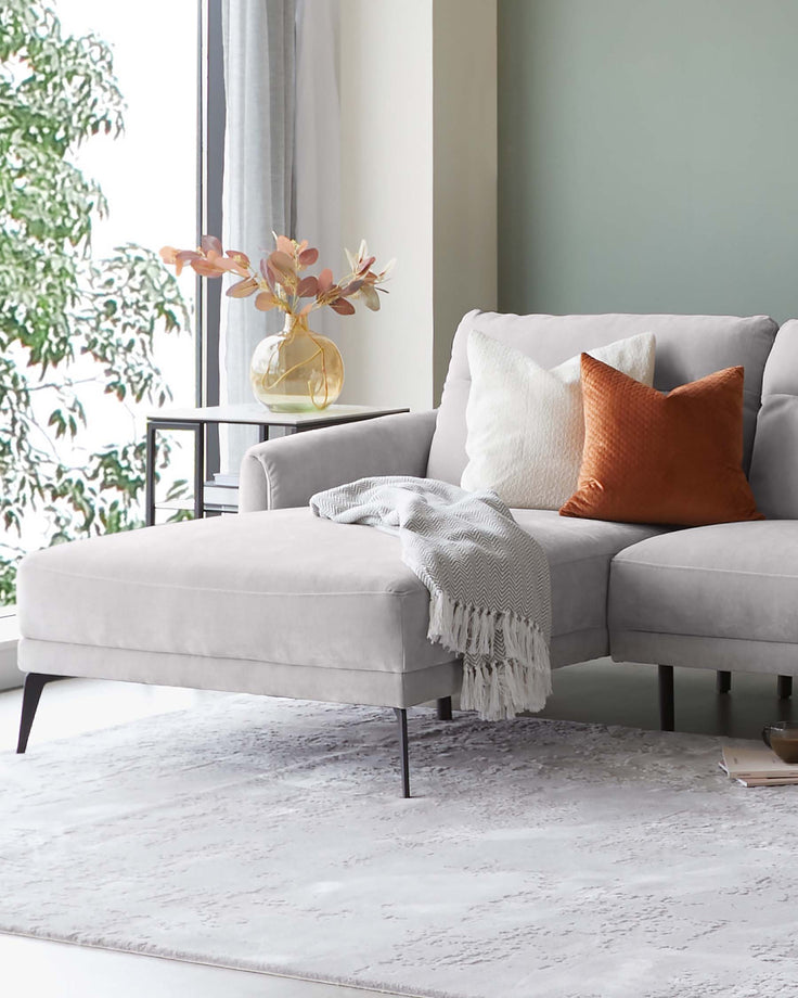 Cozy gray sectional sofa with decorative pillows, a soft throw, side table with a vase, and an elegant rug.