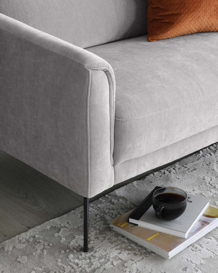 Contemporary light grey fabric sofa with clean lines and minimalist black metal legs, paired with soft textured carpet and a modern coffee table hosting books and a black mug.