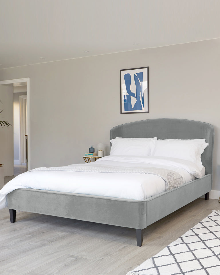 Modern grey upholstered platform bed with a curved headboard and neutral bedding, complemented by a simple white and grey area rug on a light wooden floor.