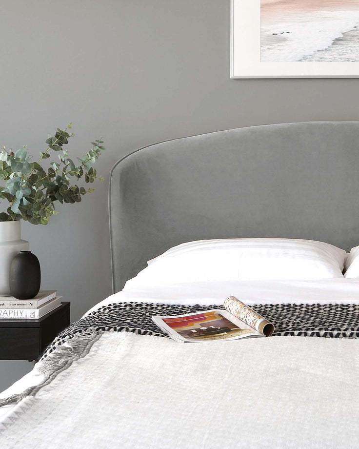 Elegant contemporary bedroom featuring a plush upholstered bed with a curved headboard in a soft grey fabric, complemented by a sleek black bedside table with clean lines and a minimalist design.
