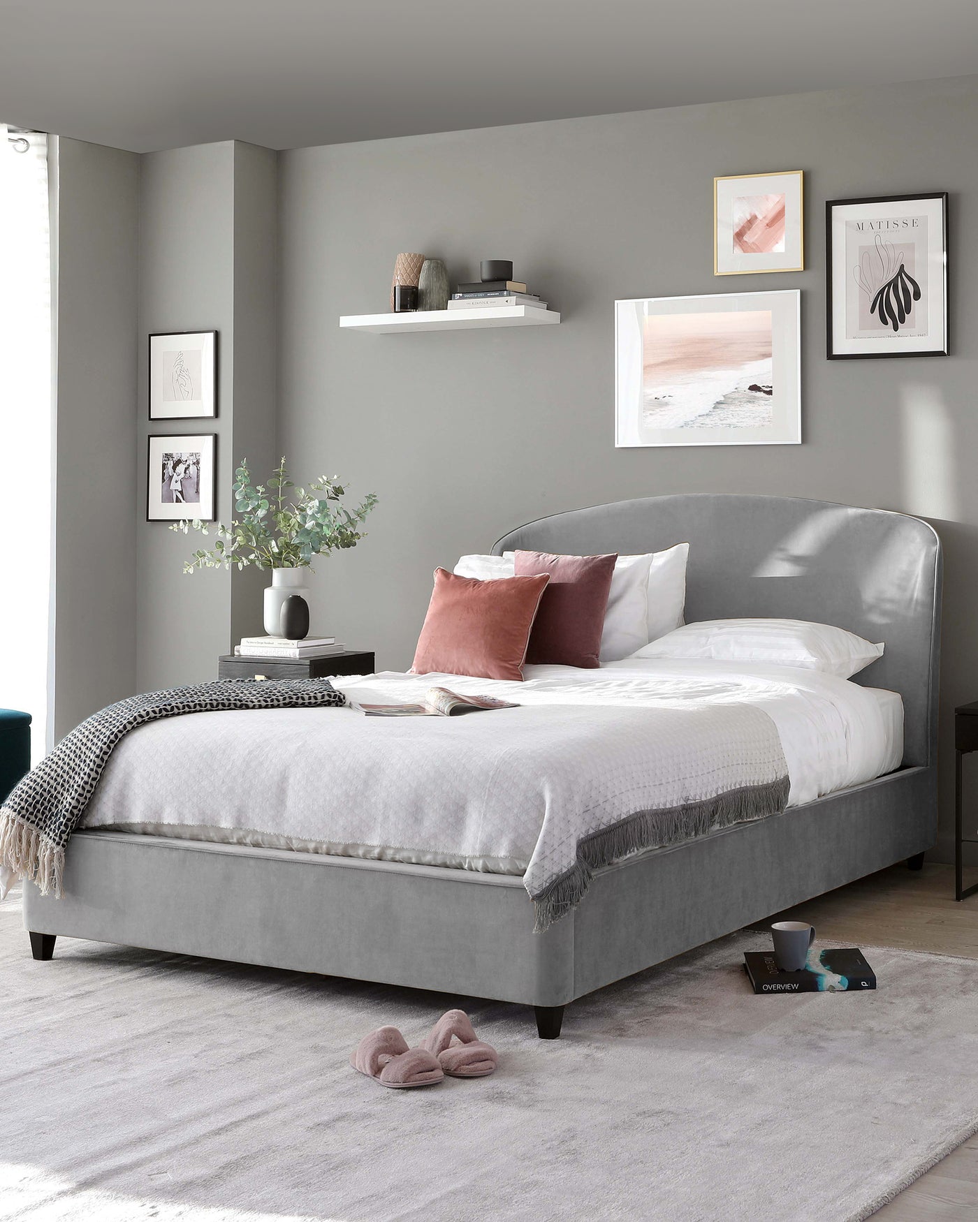 Elegant contemporary grey upholstered bed with wingback headboard design, featuring button tufting and low-profile footboard. A plush white and grey bedding set complements the bed.