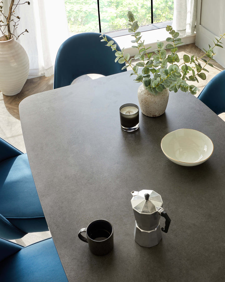 Modern matte stone grey rectangular dining table surrounded by elegant deep blue contemporary dining chairs with a minimalist design.