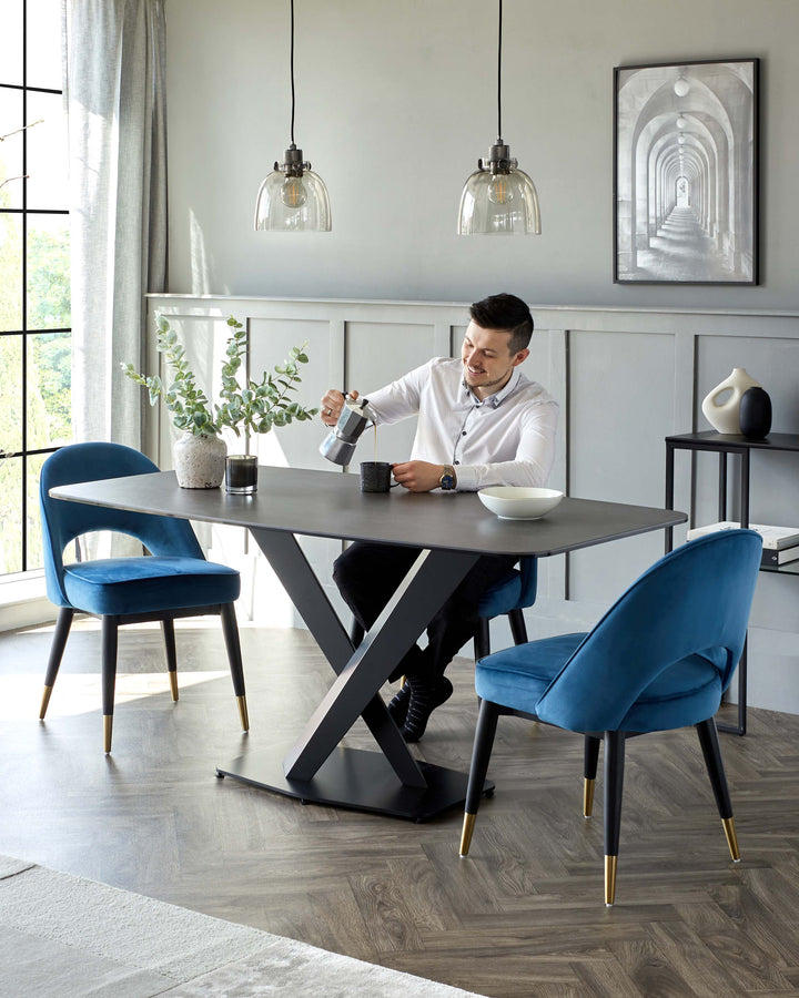 Modern dining room set featuring a square table with a dark finish and distinctive X-shaped metallic legs, paired with elegant teal upholstered chairs accented with gold-tipped legs. The ensemble showcases a blend of bold, contemporary design with a touch of luxury.