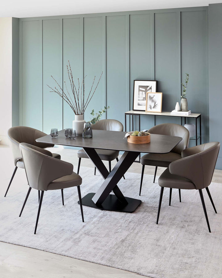Modern dining room featuring a rectangular table with an X-shaped black base and a dark wooden top, surrounded by six taupe upholstered chairs with slender black metal legs, all resting on a light grey area rug. A minimalist black console table with framed artwork and decorative vases is visible in the background.